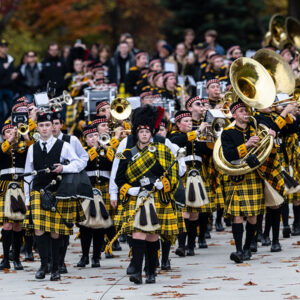 ɫƵ marching band marches in uniform with alumni and families trailing behind.